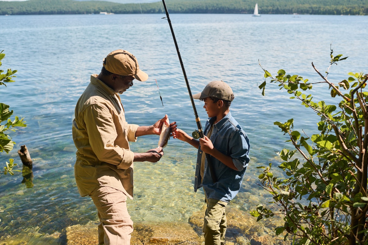 Man and his son looking at a fish that they caught in front of a lake