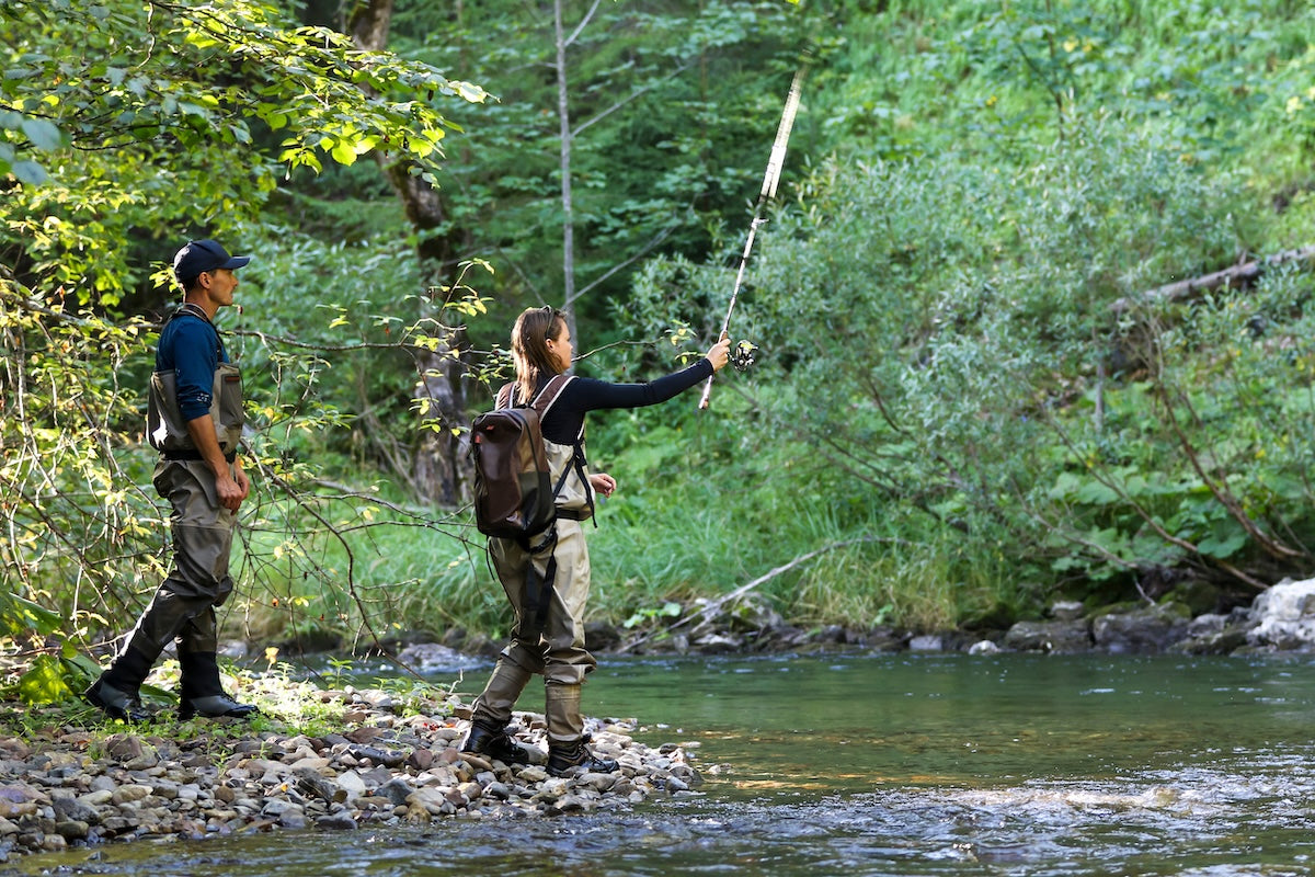 Two professional fishers walking along a creak with fishing poles